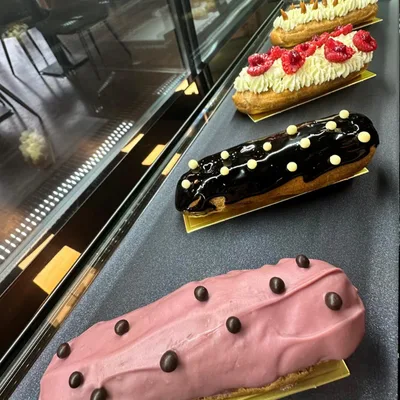 Drie eclairs naast elkaar: een met room en frambozen, een met donker chocoladeglazuur en een met roze glazuur