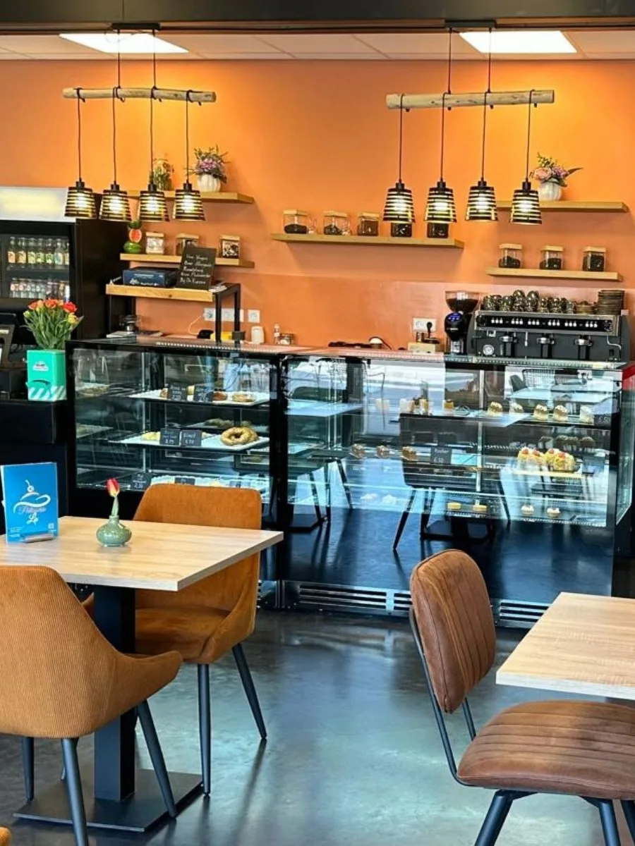 De zaal van Patisserie La met houten tafels en de verlichte vitrine